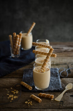 High angle in appetizing nougat mousse dessert in glasses decorated with striped wafer rolls and nuts and served on wooden table in kitchen