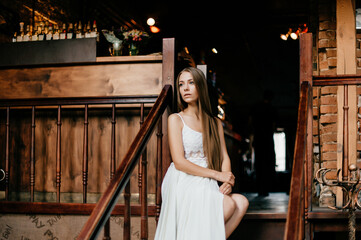 Young romantic thoughtful girl in long white dress sitting on the stairs