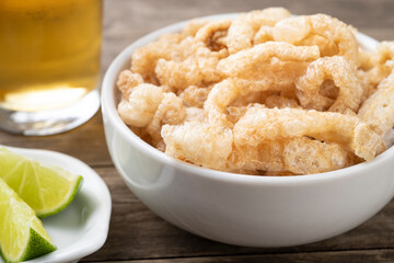 Fried pork cracklings on a white bowl with lemon and beer over wooden table