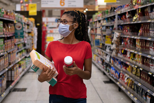 Afro latina young woman wearing a face mask walks aisle and looks at products while shopping in supermarket