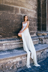Young romantic elegant girl in long white dress posing over stone ancient wall