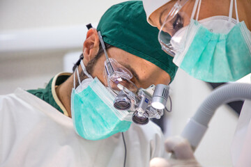 Dentists in masks and uniform operating patient lying in dental chair in bright modern clinic