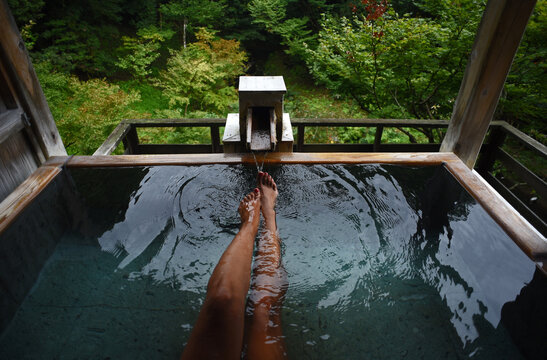 Legs and feet of caucasian female traveler enjoying a thermal waters bath in Japanese onsen, view from above