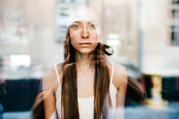 Portrait of young beautiful romantic brunette girl with long hair posing behind glass