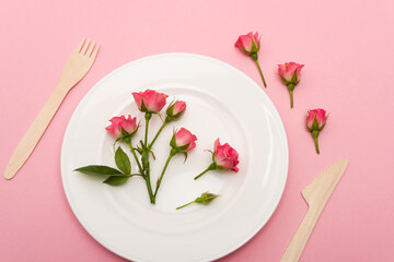 top view of wooden cutlery near white plate with flowers isolated on pink