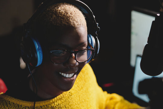 Cheerful black woman in headphones working in broadcast station and speaking in modem microphone