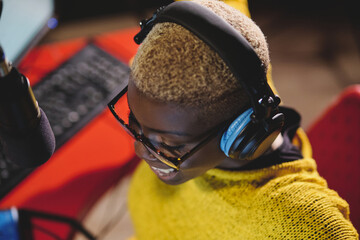 From above smiling african American female radio host working in dark broadcast studio and speaking in microphone