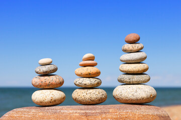 Fototapeta na wymiar Three Rock Zen pyramid of balanced stones on a background of the summer sea and blue sky