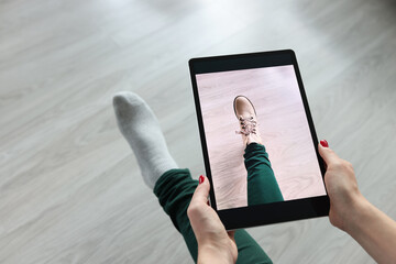 Woman holding tablet over her leg and trying on shoes closeup