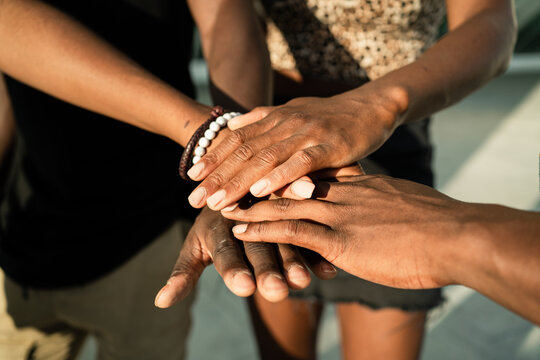 High angle of crop unrecognizable African American company of friends stacking hands together on street on sunny day