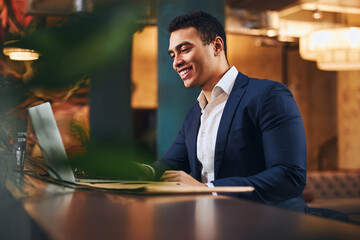 Joyful dark-haired male teleworker using his laptop