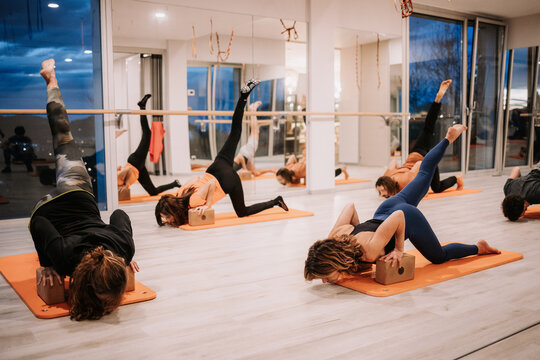 Company of people in sportswear practicing yoga on bricks and mats in Eka Pada Adho Mukha Svanasana in spacious studio in evening