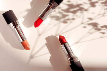 Fashion colorful lipsticks sun shadows from flowers on beige background flat lay top view. Beauty...
