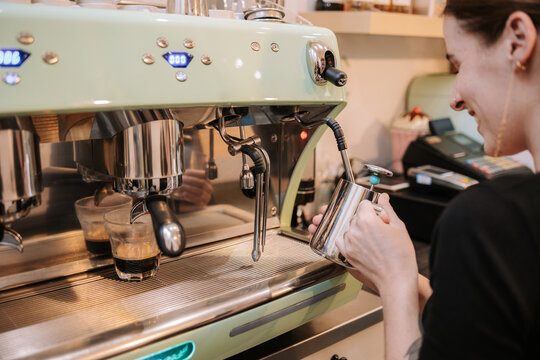 Side view of female cafe worker using coffee machine while preparing hot drink for order