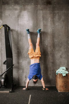 Upside down view of athletic man in protective mask performing handstand near wall in modern gym during workout