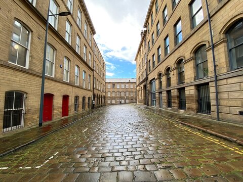Wet stone cobbles, with Victorian Yorkshire sandstone buildings on, Cater Street, Little Germany Bradford, UK