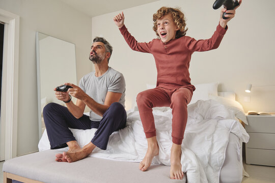 Excited man and boy with joysticks playing video games at home while having fun and spending time together