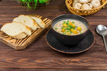 A bowl of homemade mushroom puree soup with herbs and bread on a wooden table. Homemade vegetarian mushroom soup with vegetables and bread.
