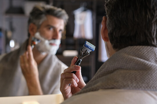 Stock photo of middle aged man with grey hair using shaving cream to shave his beard.