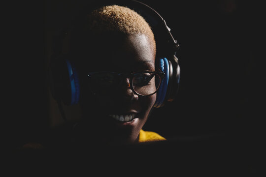 Cheerful black woman in headphones working in broadcast station and speaking in modem microphone