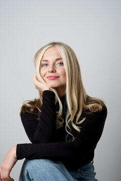 Cheerful blonde female in casual apparel sitting in studio and laughing sincerely while looking at camera