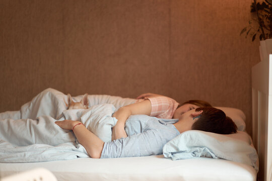 Loving couple of lesbian females lying in bed under blanket while sleeping in morning at home