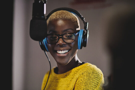 Cheerful black woman in headphones working in broadcast station and speaking in modem microphone