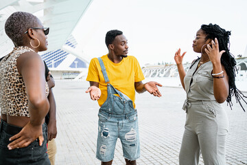 Young African American friends arguing with each other while actively gesticulating and standing on street