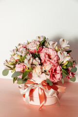 Bouquet with pink anemones and roses and eucalyptus branches in round pink box. Satin ribbon on the box. Present, spring time, happy women's day. On white background.