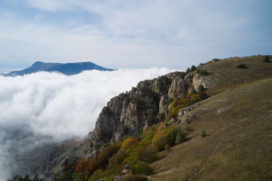 From above drone view of picturesque landscape of rocky mountains with green slopes covered by thick white clouds in sunny autumn day