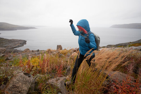 Side view of female hiker in warm clothes and with backpack trekking in rocky terrain on cloudy weather near sea