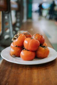 Pile of fresh ripe delicious persimmon fruits arranged on white plate placed on wooden counter in food market