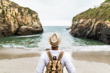 Back view of anonymous male traveler standing on sandy coast enjoying freedom during summer vacation near sea