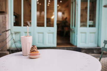 Yummy cupcake and glass of drink served on round table placed on terrace of cozy confectionery cafe
