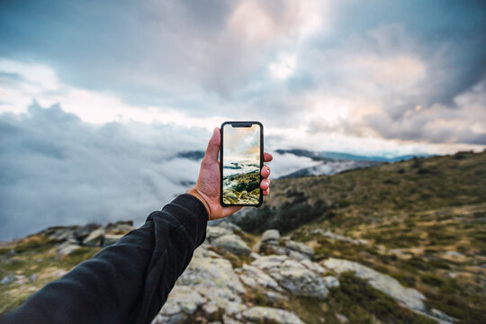 Hand of unrecognizable crop hiker standing in rocky terrain and taking photo of incredible mountain landscape while using mobile phone