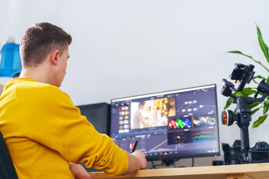 Side view, the guy-videographer using a pen-tablet and a special program makes video processing on the front computer at home. Video editing. Blogging. Freelancer. Remote work. Retouching training