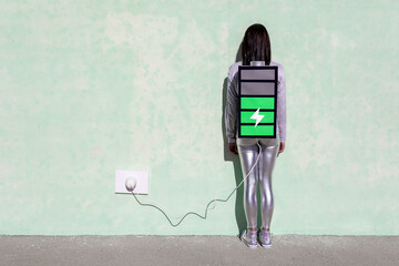 Back view of unrecognizable female with long dark hair in stylish outfit standing on street near wall with battery shaped backpack connected to charger