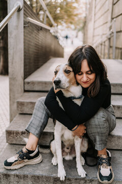 Side view of female owner gently embracing Treeing Walker Coonhound dog while sitting on street in city