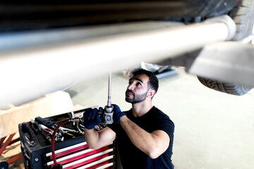 Busy male technician using special instrument and fixing car while working in modern service