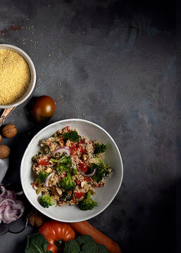 Top view of bowl with healthy homemade bulgur couscous salad with various vegetables and walnuts served on table with ingredients