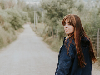 chica pelirroja mirando fijamente, vestida con una chaqueta azul en medio del camino en el campo.