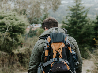 joven joven de espaldas esta caminando dentro del bosque por un pequeño sendero con una maleta de viajes