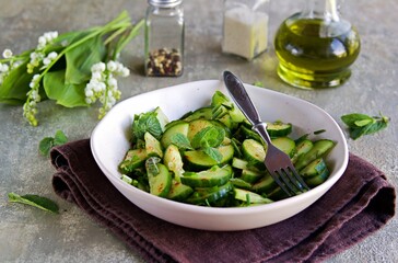 Fresh salad of cucumbers, green onions and fresh mint in an clay plate on a gray concrete background. Cucumber recipes.