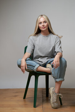 Young Cool Female In Stylish Outfit Sitting On Chair On Gray Background And Looking At Camera