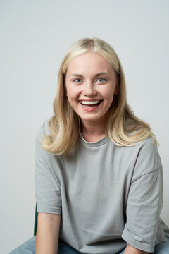 Cheerful blonde female in casual apparel sitting in studio and laughing sincerely while looking at camera