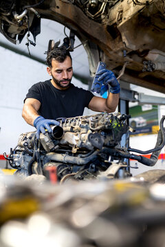 Serious male mechanic with flashlight examining lifted car while working in automobile service