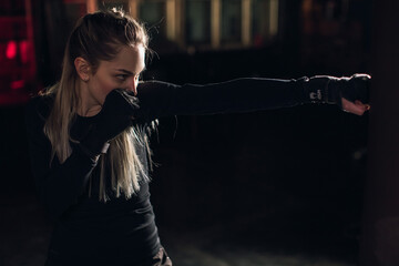 Cool female fighter in boxing bandages trains in gym. Mixed martial arts