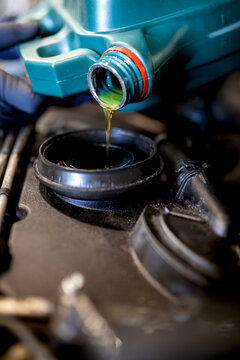 Serious Male Mechanic Pouring Engine Oil In Motor Of Car While Working In Repair Service