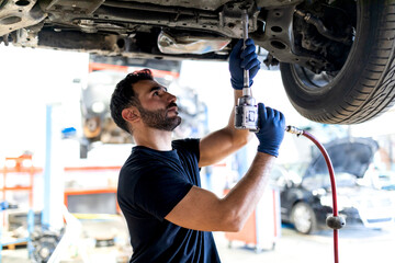 Busy male technician using special instrument and fixing car while working in modern service