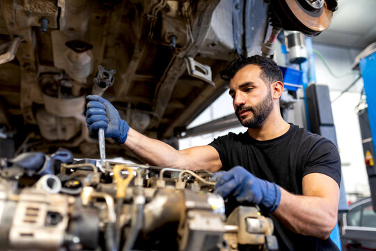 Busy bearded male mechanic with metal wrench repairing dirty car engine in modern service